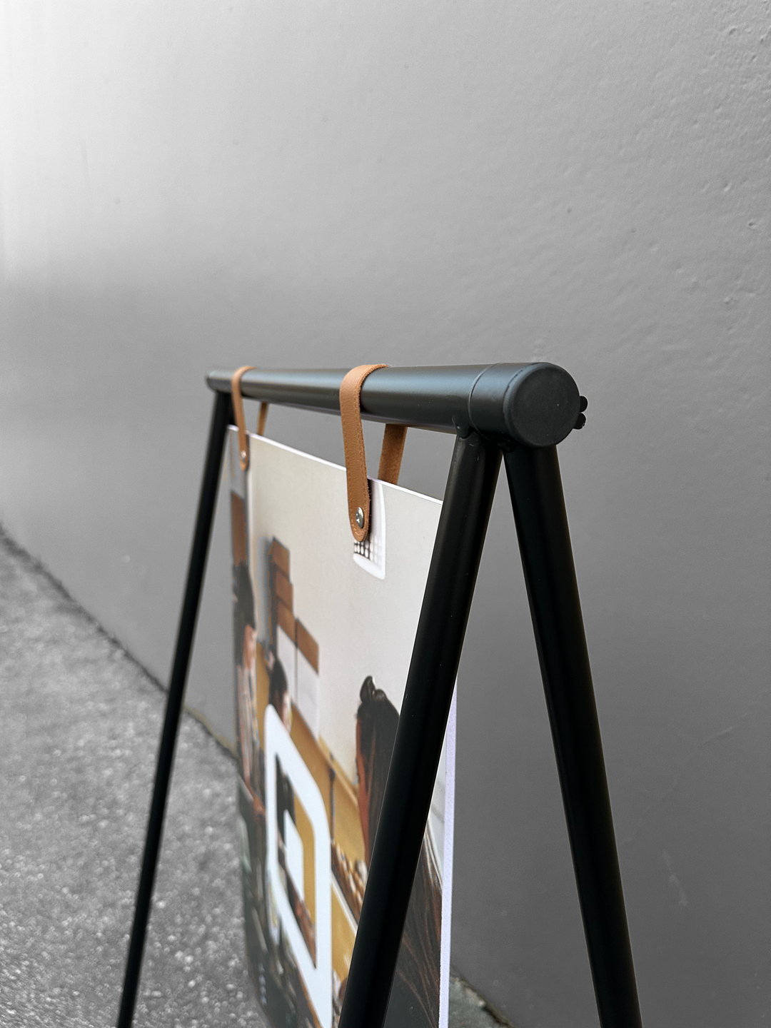 Black metal stand holding a poster against a gray wall